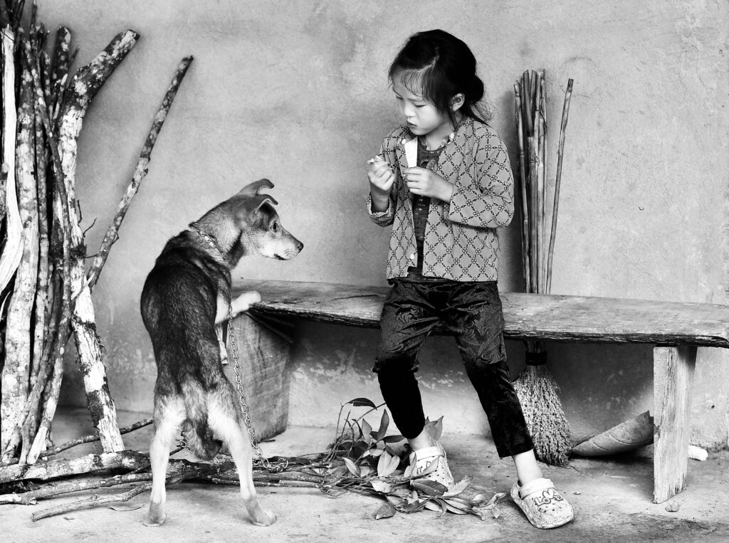 Black and white photo of a child undergoing NET therapy, gently playing with a dog during a therapeutic session.