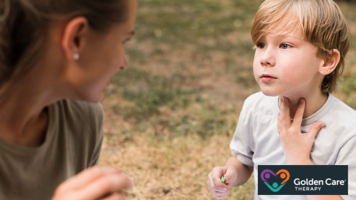 A blonde boy with autism receives guidance from a female therapist in an open field with dried grass.