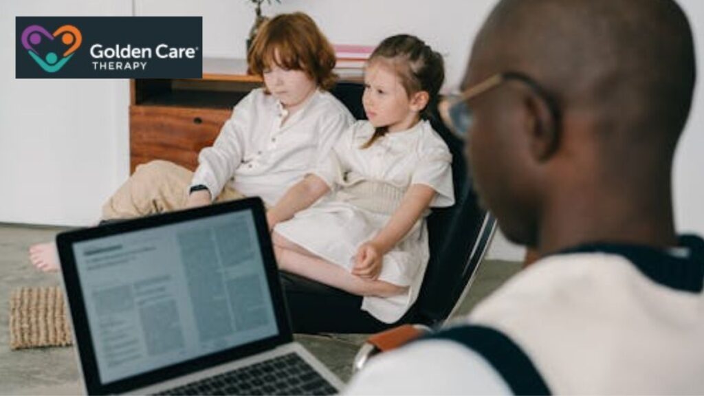 Autism behavioral therapy session with a male therapist, seen from behind, talking with two children during a clinic-based session.
