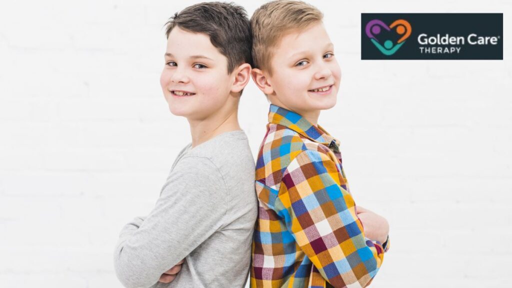 Two boys, one with autism and one with ADHD, stand back-to-back against a white wall, looking directly at the camera.