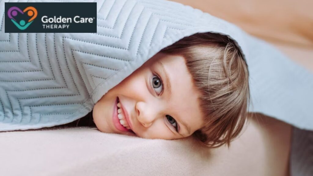 A young girl looks at the camera from under a heavy weighted blanket, enjoying its cozy, comforting feel.