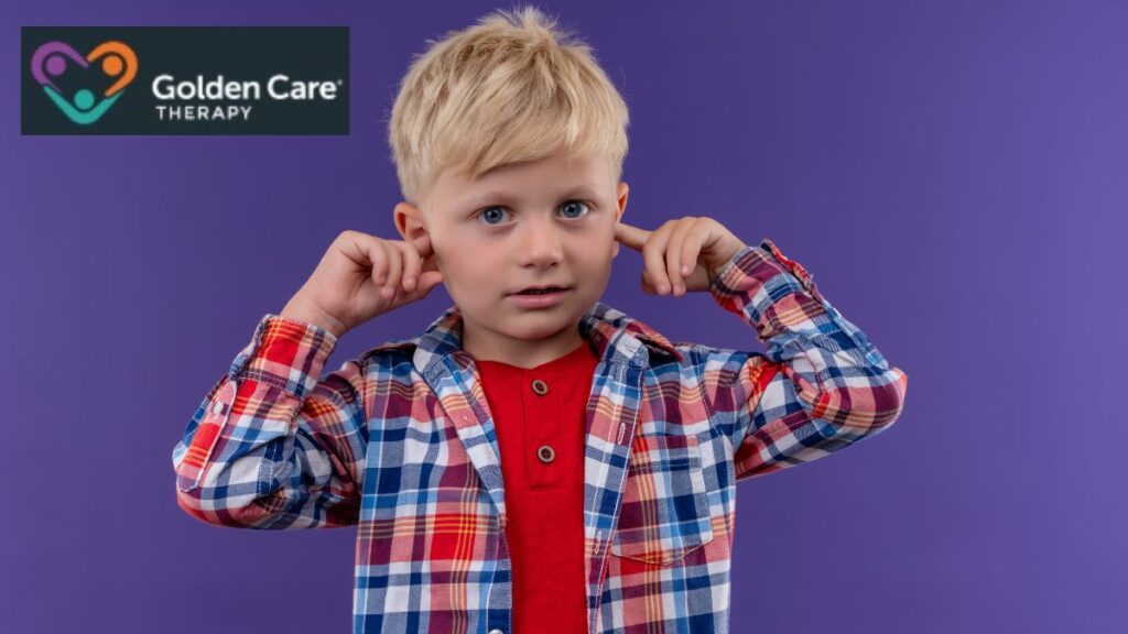 A young boy in a checkered shirt plugs his ears with his fingers against a violet background, illustrating tone deafness and sound sensitivity in autism.