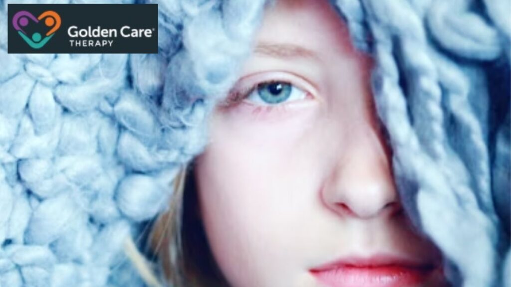 A young girl stares at the camera with a blue blanket draped over her head like a hood, enjoying its cozy, calming comfort.