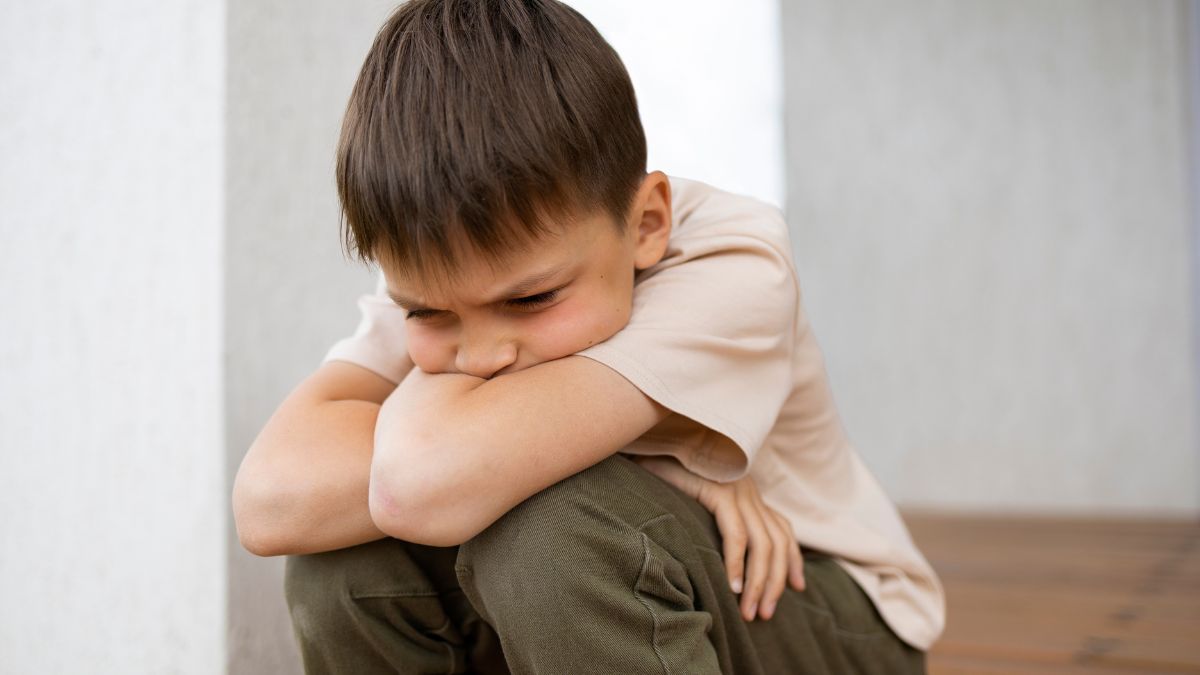 Discrimination and autism, a young boy sits outdoors hunched down and alone.