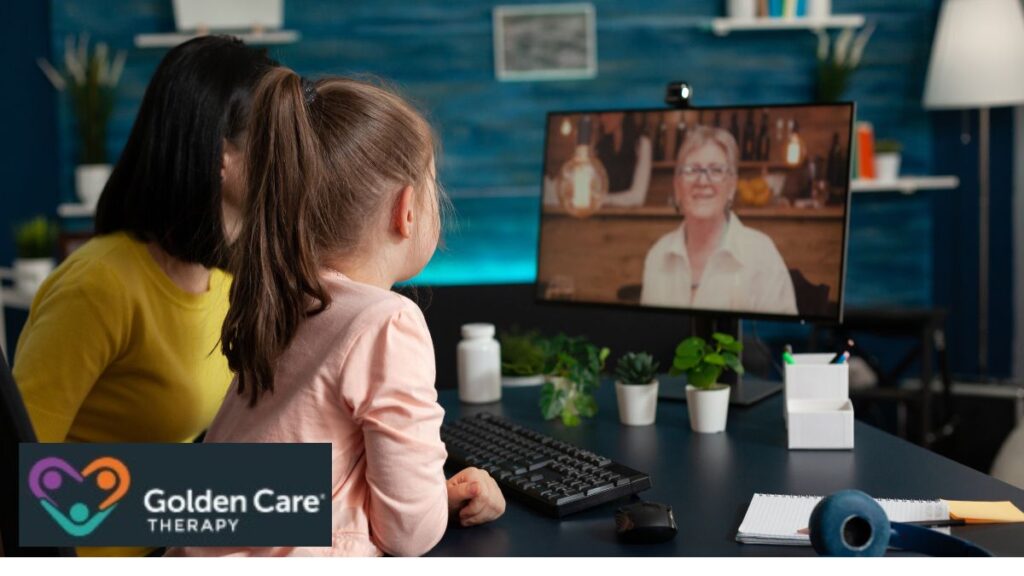 A young girl and her adult caregiver sit together in front of a computer, actively participating in an online ABA therapy session with a therapist visible on the screen.