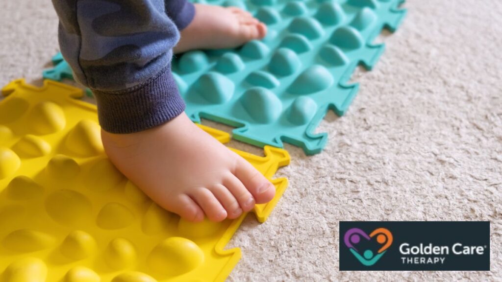 A toddler stands on a textured, colorful surface as a sensory-seeking, self-soothing alternative to rubbing their feet together, a common behavior in autism.