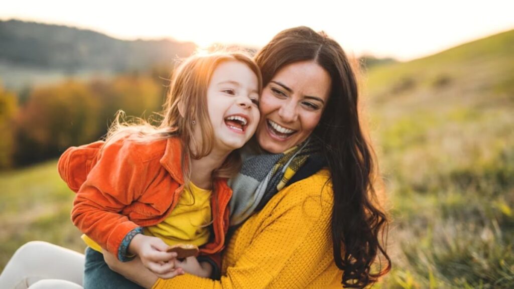 A mother and her autistic daughter share a joyful embrace in a sunlit meadow, warm light surrounding them as they smile with pure happiness.