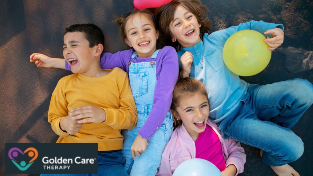 A group of children sit huddled together on the floor, one boy holding a balloon as they share laughter and camaraderie during a playful game.