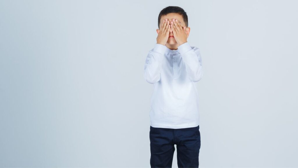 A young boy covers his ears and shows a look of extreme discomfort, struggling with sensory overstimulation.