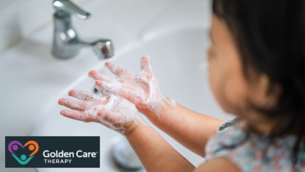 A girl, seen from behind in a top view, washes her hands with soapy water at a faucet as part of an autism visual-aid activity.