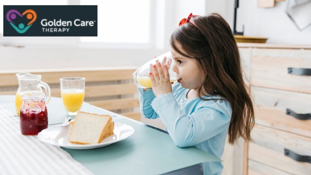 A child drinks fruit juice at breakfast, sitting at a table with other breakfast items, following a daily visual schedule.