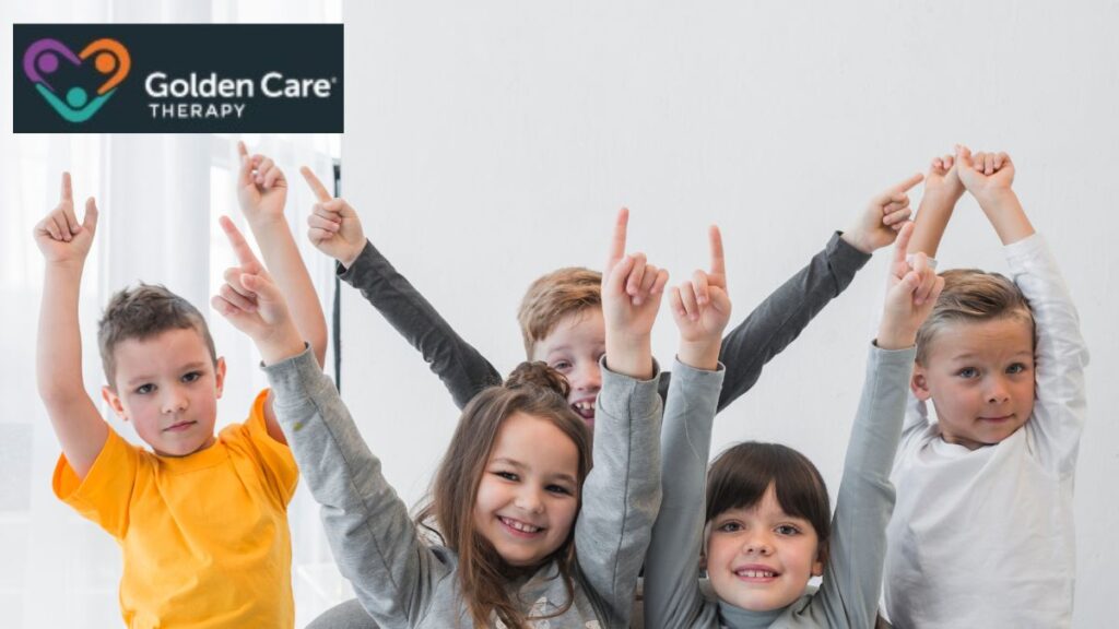 A group of children smile joyfully at the camera, their arms raised and fingers pointing upward in a moment of shared excitement and happiness.