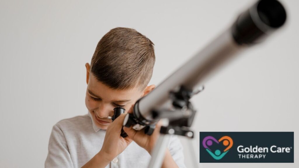 A young boy peers through a telescope in a white room, aiming it toward the sky outside.