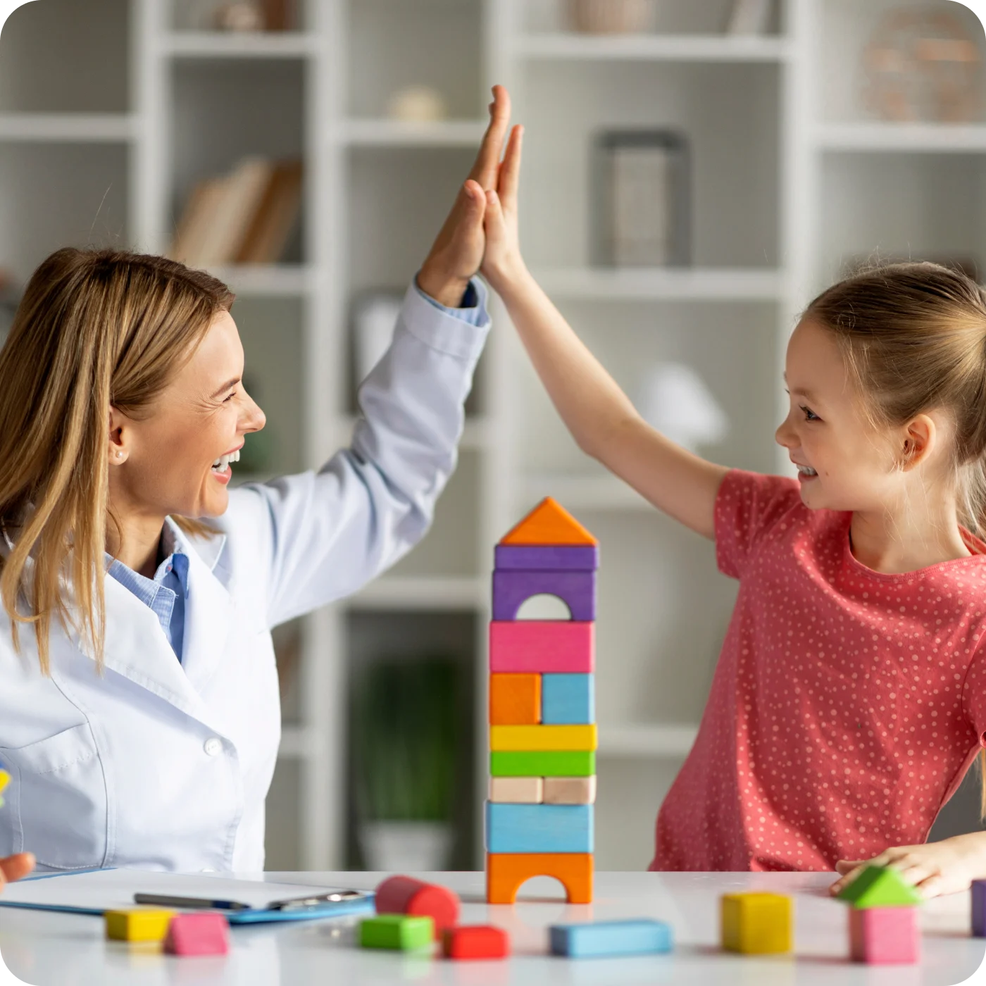 Therapist and child high-five beside colorful building blocks